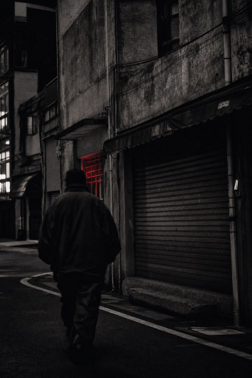 Figure in an oversized jacket walking through a back alley at dusk